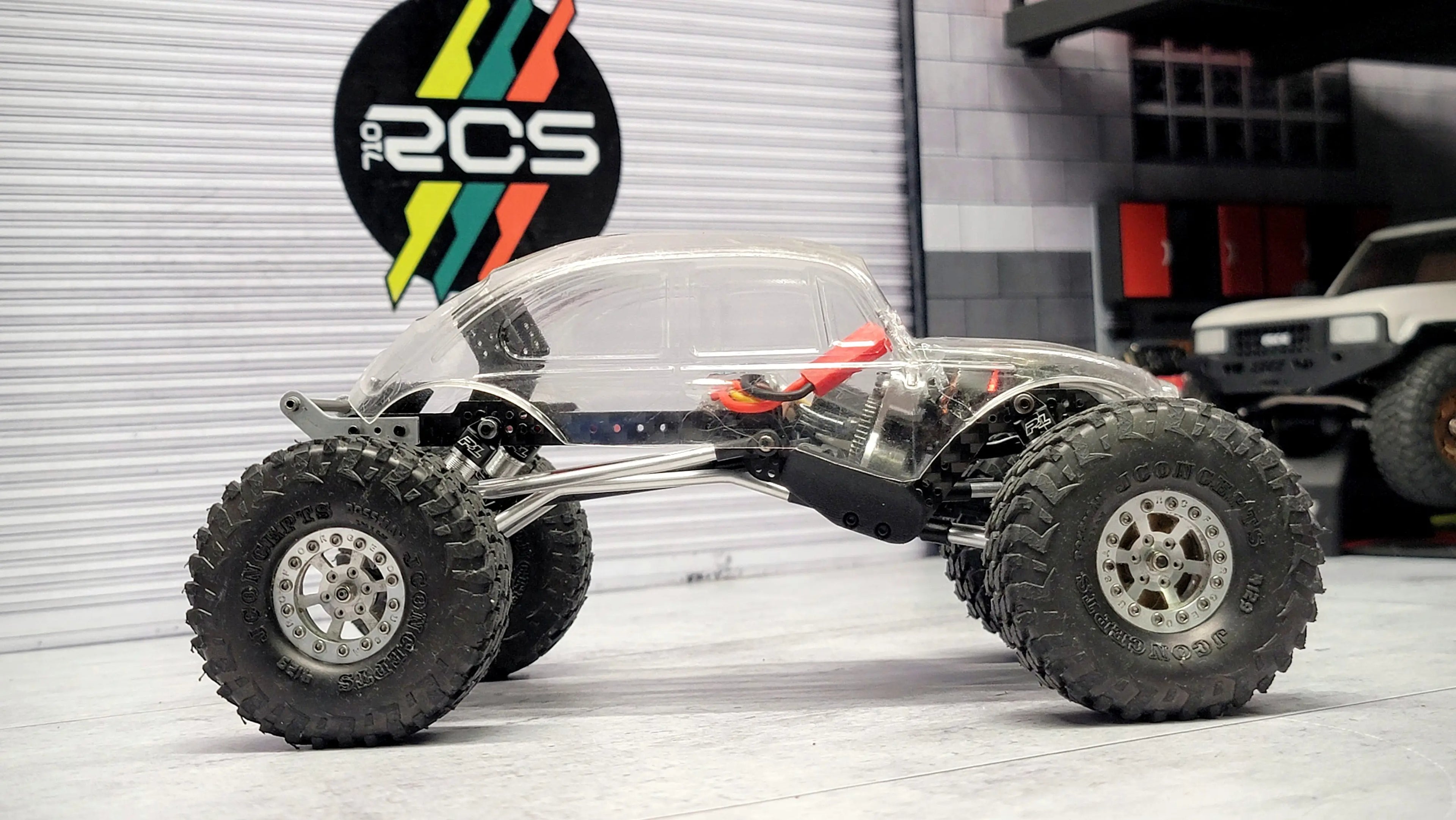 RC crawler with clear polycarbonate body and titanium links on display in RCSTEVE workshop, highlighting chassis engineering and setup.